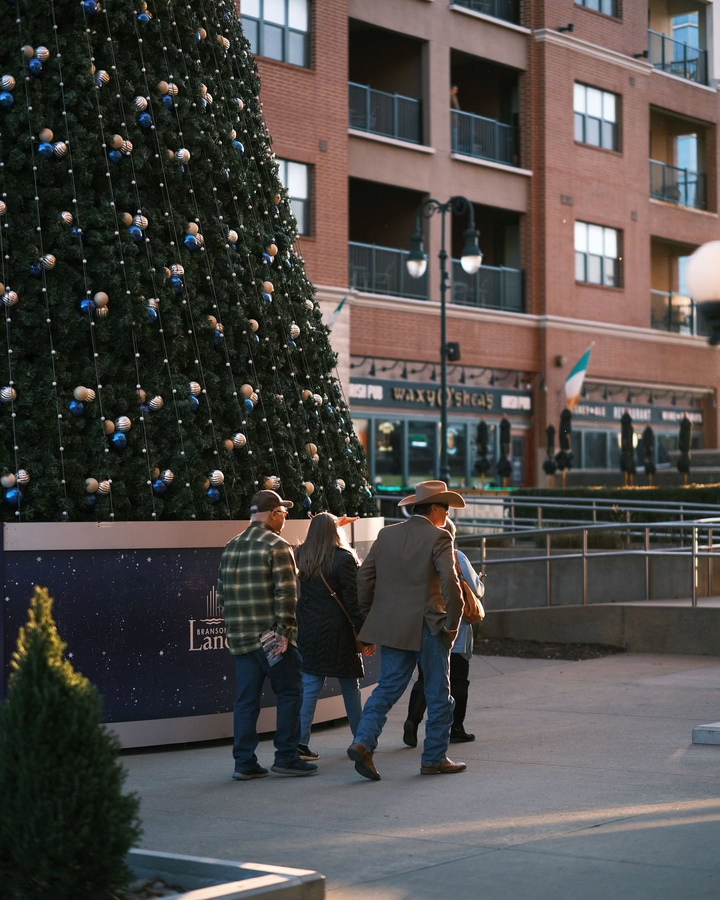 Street shot of people walking past a lit Christmas tree at Branson Landing.