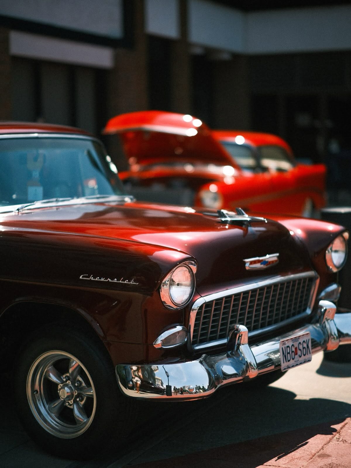 Close-up of a classic maroon Chevrolet at a car show, hoods up on the cars behind it.