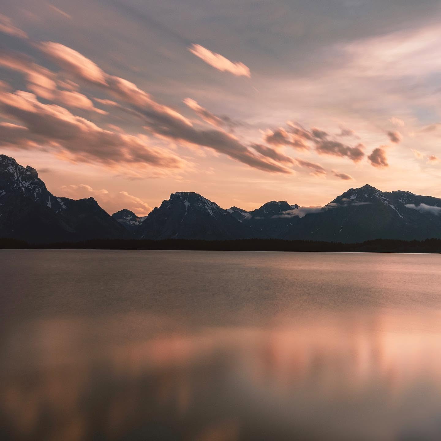 Long-exposure landscape shot of the Tetons at sunset, reflected in the lake below.